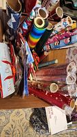 Photo showing a variety of rolls of wrapping paper upright in a box including Christmas patterns, rainbow stripes, and other miscellaneous prints.