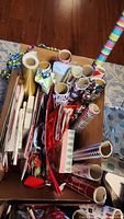 Top view of the box containing multiple rolls of wrapping paper, gift bags, gift boxes, and curling ribbons seen inside the box.