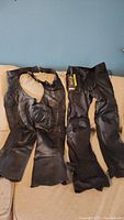 Pair of black motorcycle pants and leather chaps displayed side by side showing their full length