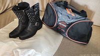 Black leather ladies Harley Davidson boots with studs and buckle details next to Harley Davidson branded duffel bag