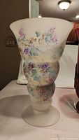Photo showing large frosted glass vase with hand painted purple and blue flowers and leaves on a curvy body and flared rim.