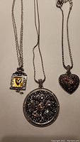 Three silver tone Brighton necklaces displayed on a surface showing pendants and chains.