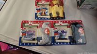 Full view of three Ty Beanie Babies in original packaging on white surface: Liberty the Bear, Righty the Elephant, and Lefty the Donkey with patriotic-themed packaging.
