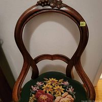 Close-up of chair seat and balloon back with floral needlepoint upholstery and carved wood detail.