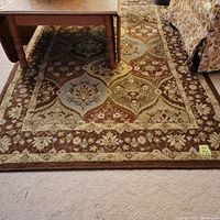 Rug under wooden table with floral upholstered chair on side; showing overall pattern and condition.