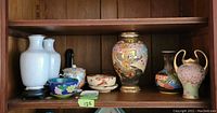 Wide view of shelf showing all 8 items including cloisonne and porcelain vases and bowls.