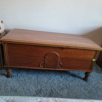 Closed front view showing wooden chest with diamond embellishment and carved front details, standing on round legs.