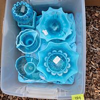Top view of blue and milk glass pieces including hobnail patterns, pitchers, bowls, and vases arranged in plastic bin.