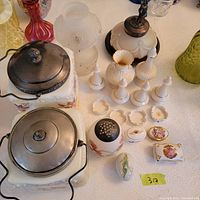 Lot arranged on table showing porcelain biscuit jars with lids, salt and pepper shakers, trinket boxes, small coaster plates, frosted glass vases, and vintage lamp with figurine top.