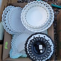 White and black milk glass plates and bowls stacked inside a cardboard box showing ribbon edge design on each piece.