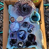 Overhead photo of lot showing all pieces arranged in a box on white fabric, showcasing purple slag glass items and purple lusterware.