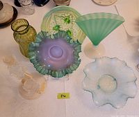 Overview of the lot showing all art glass pieces including bowls, vase, candlesticks, and decorative dish on a white textured tablecloth.