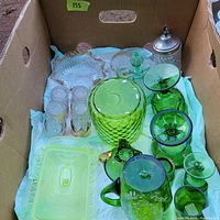 Photo of boxed assortment of various glassware items including green and yellow depression glass, clear glass with patterns, and a jar with metal lid.