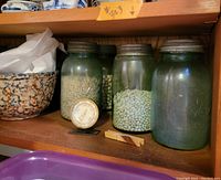 Four vintage Ball mason jars filled with various dried legumes; a small metal thermometer is visible near the jars.