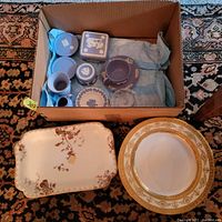 Lot of blue Wedgwood Jasperware items including bowls, containers, a covered box, along with porcelain plats and serving trays placed in cardboard box and on the floor.