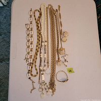 Top view of multiple cream and gold toned vintage jewelry pieces laid out on white surface including necklaces, earrings, bracelet, and ring.
