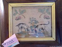 Front view of the antique wood framed needlepoint art showing two spotted dogs near a tree with leaf and berry details.
