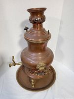 Front angle view of vintage copper and brass samovar teapot on matching round copper plate, showing lion head detail and spout.