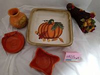 Vintage fall-themed ceramic dishes with pumpkin design and small orange dishes alongside a small ceramic vase and a decorative cornucopia.