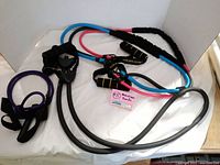 Photo showing four resistance bands in purple, gray, blue, and pink, folded with black foam-grip handles and ankle straps