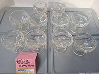 Top view of all ten glass ice cream dishes showing their rounded bowls, short stems, and solid bases arranged on two trays.