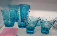 Seven aqua blue bubble glasses and one bowl, plus one clear Anchor Hocking tumbler glass, shown on shelf.