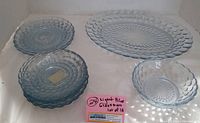 Photo showing multiple blue glass plates and bowls with bubble textured pattern, light blue color, arranged in stack and display.