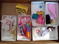 Various vintage miniature toy figurines, small dolls, fabric doll clothes and accessories in six compartments of cardboard boxes.