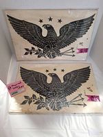 Two large black eagle decals in protective clear sleeves, showing full eagle design with spread wings, three stars, arrows, and olive branch on beige backing.