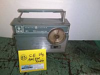 Front view of vintage General Electric AM/FM transistor radio showing the front speaker grille, tuning dial, and handle on top.