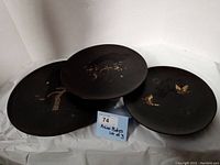Three round black serving plates with gold-tone Asian designs, arranged together showing front side details.