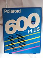 Close-up photo of front face of blue Polaroid 600 Plus radio showing model name, Polaroid logo, speaker grille and colored stripes.