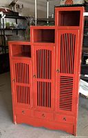 Front view of red stepped cabinet showing three doors, drawers, and cubbies