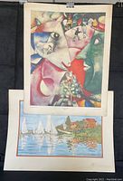 Two classical artwork prints hanging, one above the other. The top print is a colorful surrealistic piece by Chagall, while the bottom print is an impressionist scene with sailboats by Monet.
