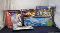 Wide shot of all five toys showing their original packaging: Explorer Talking Globe on left, two Air Hogs boxed toys in center, Falcon model plane lower front right.