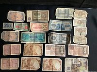 Collection of assorted foreign banknotes laid on a black surface showing various currencies from France, Germany, England with different denominations and wear conditions.