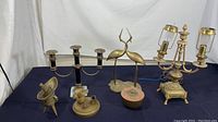 Photo showing full set of six vintage brass decor items on display including candelabra, table lamp, cranes figurine, and smaller decorative pieces