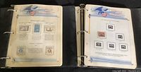 Photo of two ring binders open side by side showing U.S. commemorative stamp pages with illustrated headers and mounted stamps.
