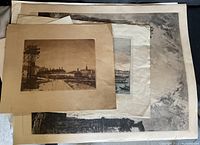 Top view of stacked vintage art prints showing various cityscapes and landmark themes with some visible wear on edges