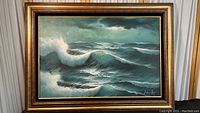 Full view of the framed oil painting showing crashing ocean waves under a cloudy sky with artist's signature in the bottom right.