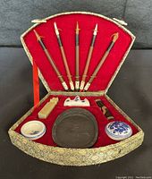 Full view of vintage Chinese calligraphy set displayed in red velvet lined ornate gold box. Includes 5 brushes, inkstone, brush rest, seal, ink container and more.