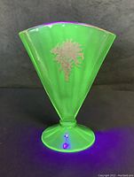 Front view of green Vaseline glass fan vase showing golden floral decoration under UV light