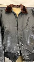 Front view of black leather flight jacket showing fuzzy collar, knit cuffs and waistband, and zipper details with some wear and shine.