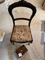 Full view of antique wooden chair with embroidered floral cushion and small sewing box on carpeted floor