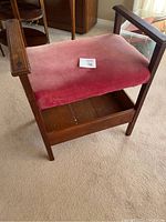 Front view of wooden sewing bench with faded red velvet seat and wooden frame.