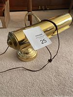 Brass desk lamp with cylindrical shade and curved support arm, showing front angle and electrical cord.