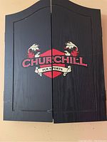 Closed front view of black wooden dart board cabinet with Churchill Pub Sports logo on the doors.