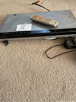 RCA DVD player with metal casing and remote control on top showing front panel with control buttons.