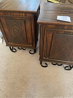 Side view showing two wooden end tables with dark stained paneled wood and iron curled feet and accents.