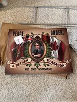 Lawn sign with Sir John A image, flags, and political slogans, laid flat on carpet with metal stand behind